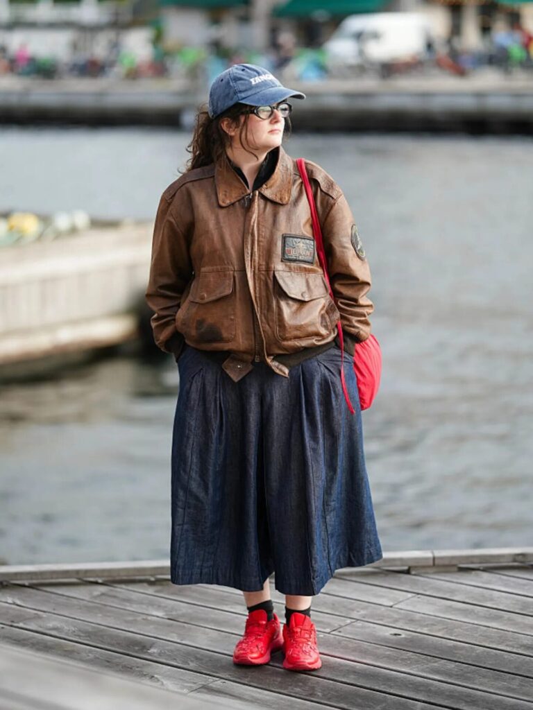 Candid shot of a person on a boardwalk in a long skirt and fall jacket, wearing bright red sneakers.