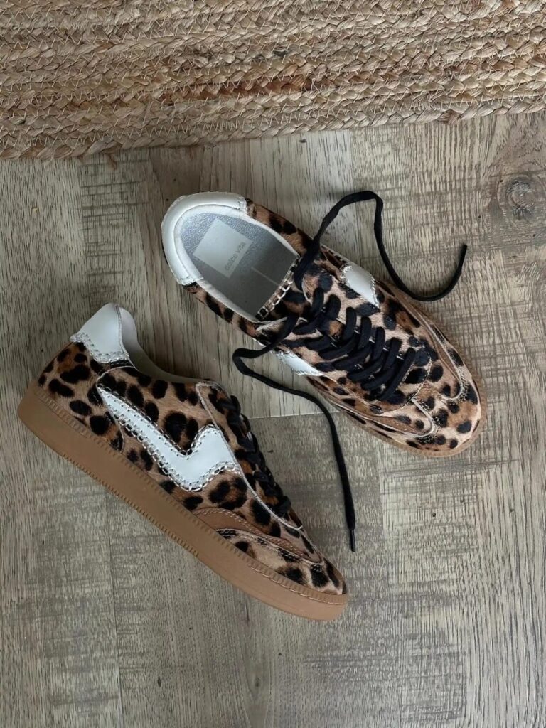 Flat lay of leopard print and snakeskin sneakers placed on a wooden floor with a woven mat.