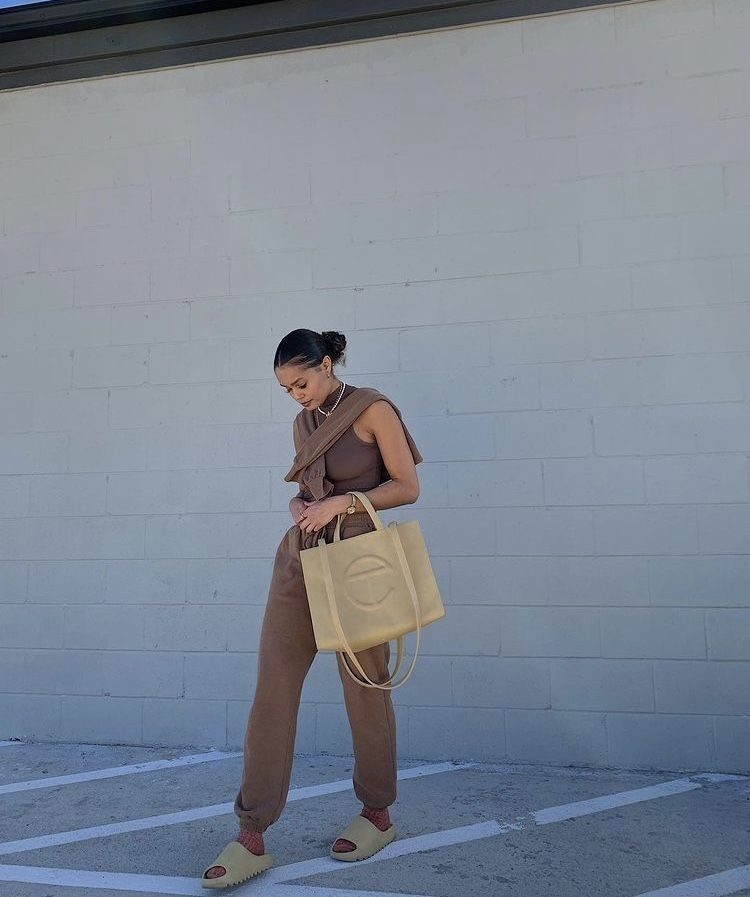 Woman at airport wearing beige monochrome travel outfit with wide-leg pants, matching top, and neutral tote bag