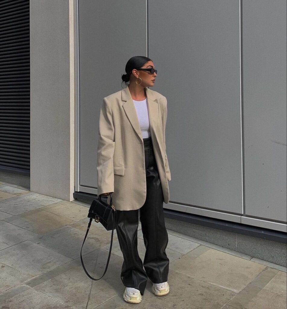 Traveler wearing soft leather pants with a white T-shirt and sneakers, rolling carry-on luggage