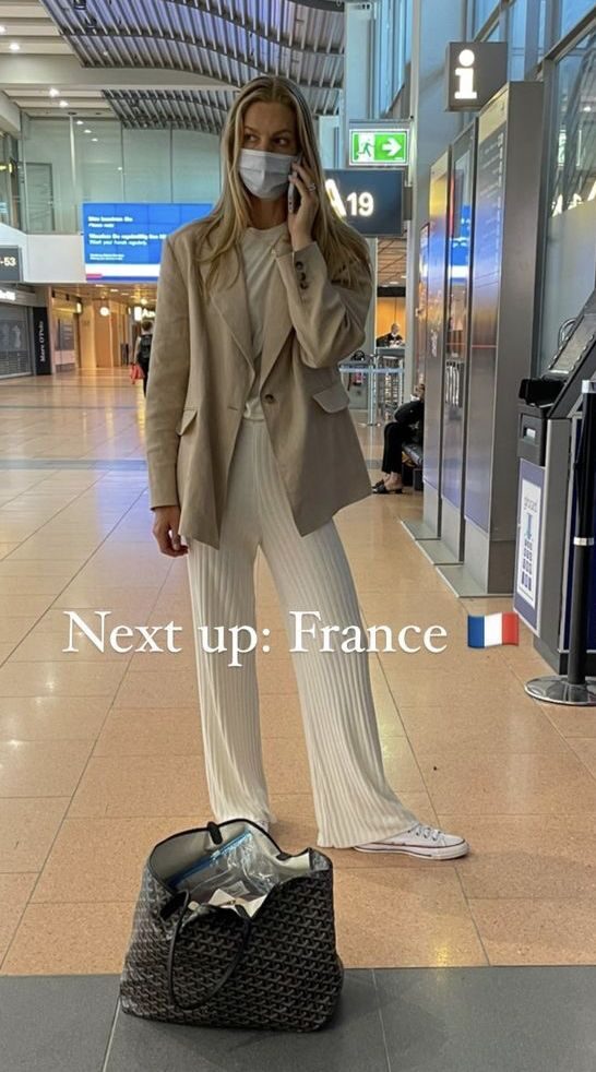Woman in soft knit pants and light blazer sitting in airport waiting area with coffee cup