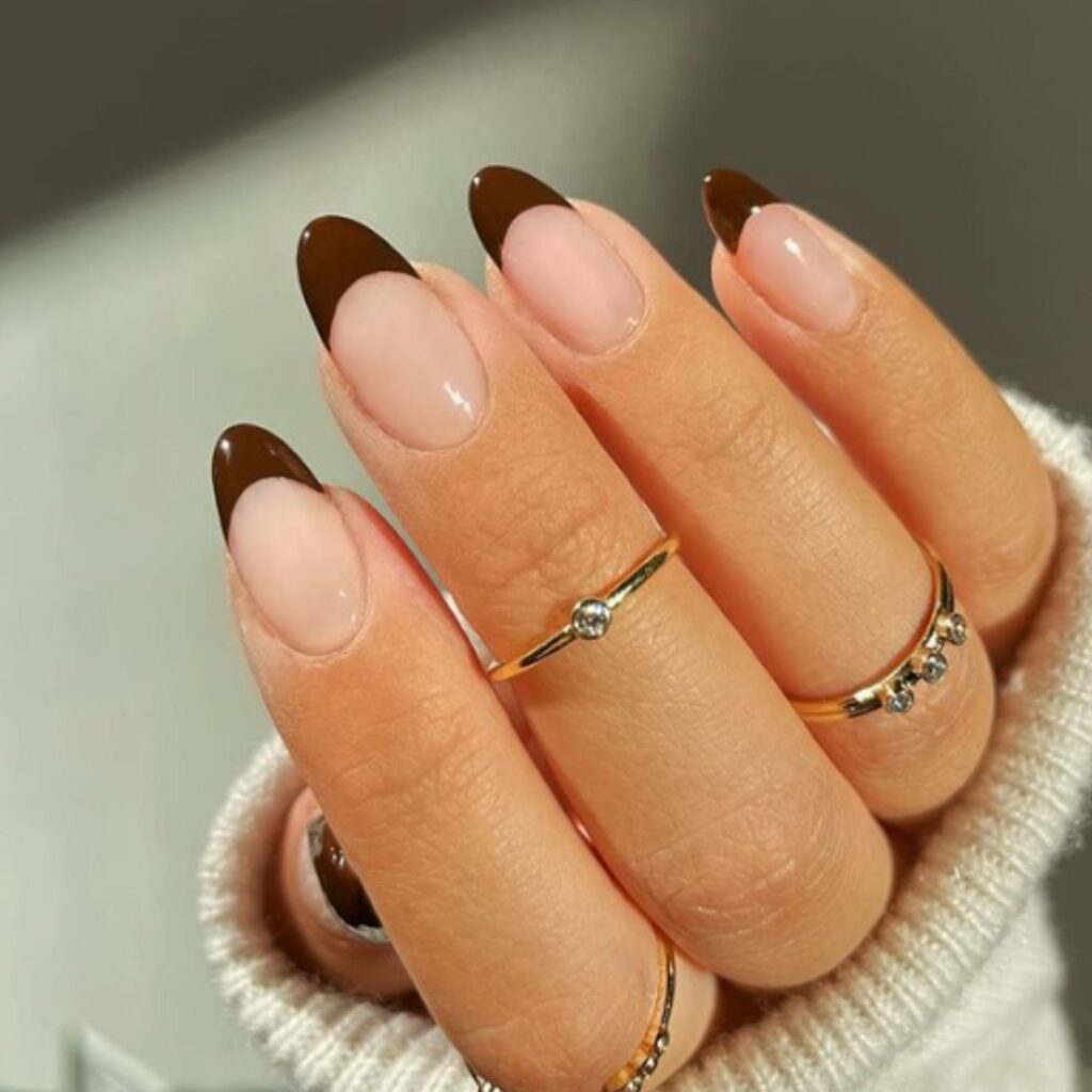 Hand with glossy deep espresso-brown nails, styled with gold rings and a soft knit sweater background.