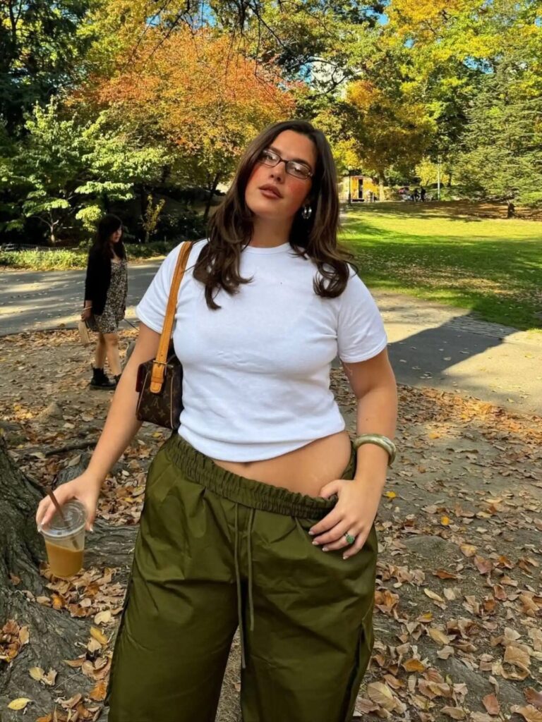 Model wearing muted olive trousers with a white tee, styled with minimalist accessories, reflecting the earthy olive color trend for fall 2025.