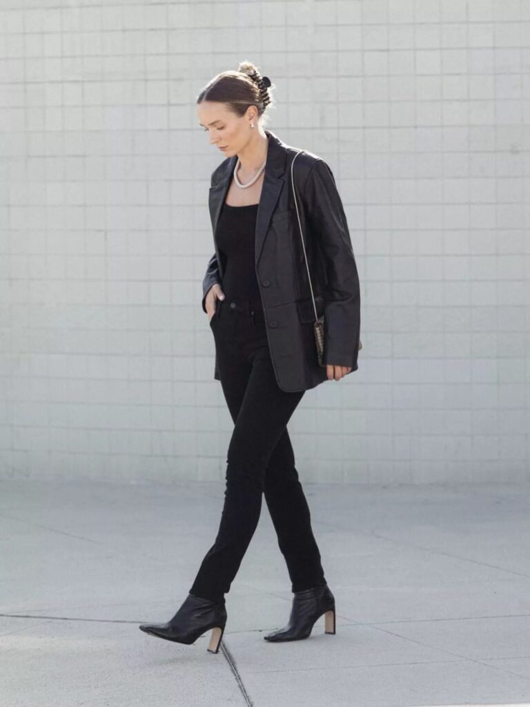 Woman wearing black skinny jeans, leather blazer, and knit bodysuit styled as a business casual black denim outfit