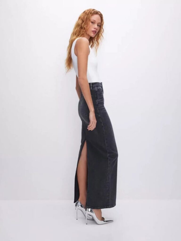 Model in a black denim maxi skirt styled with a white rib tank top and silver metallic heels for a chic spring look.