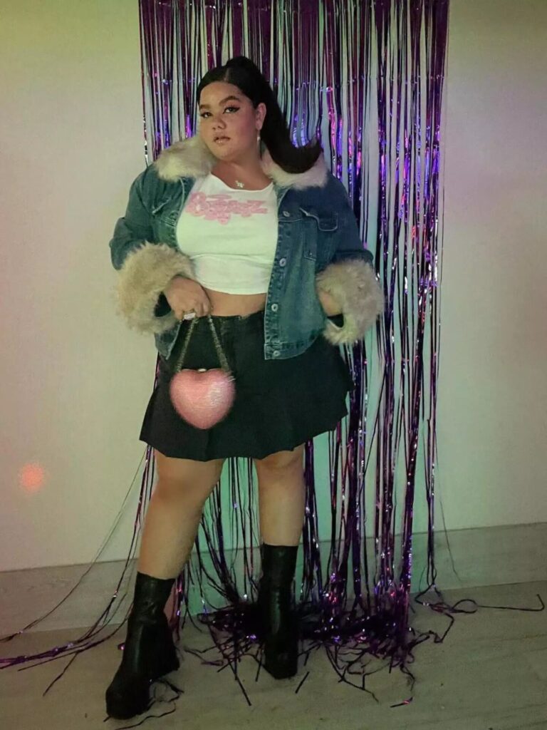 Priscilla Del Castillo wearing a black denim pleated mini skirt, Bratz tee, and fur-trimmed denim jacket with a pink heart-shaped purse