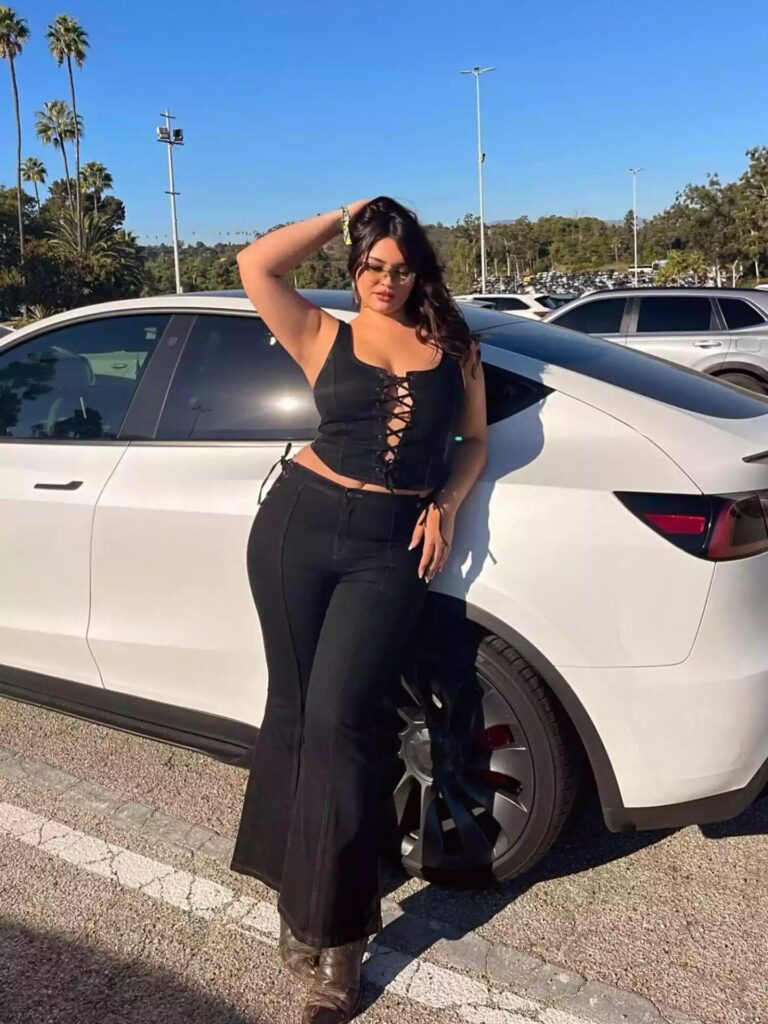 Bella Golden wearing black denim flare jeans styled with a black corset top and silver hoop earrings for a bold chic look.