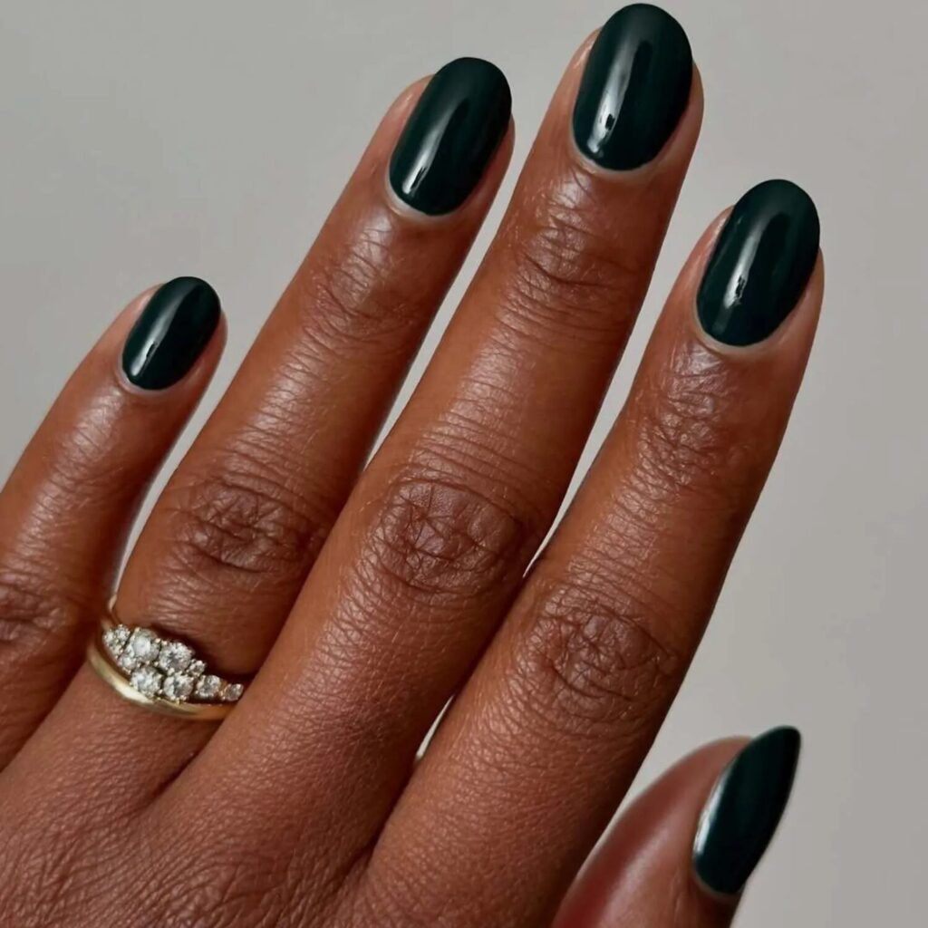Short nails painted in dark forest green polish with a gold diamond ring perfect vampy manicure for October