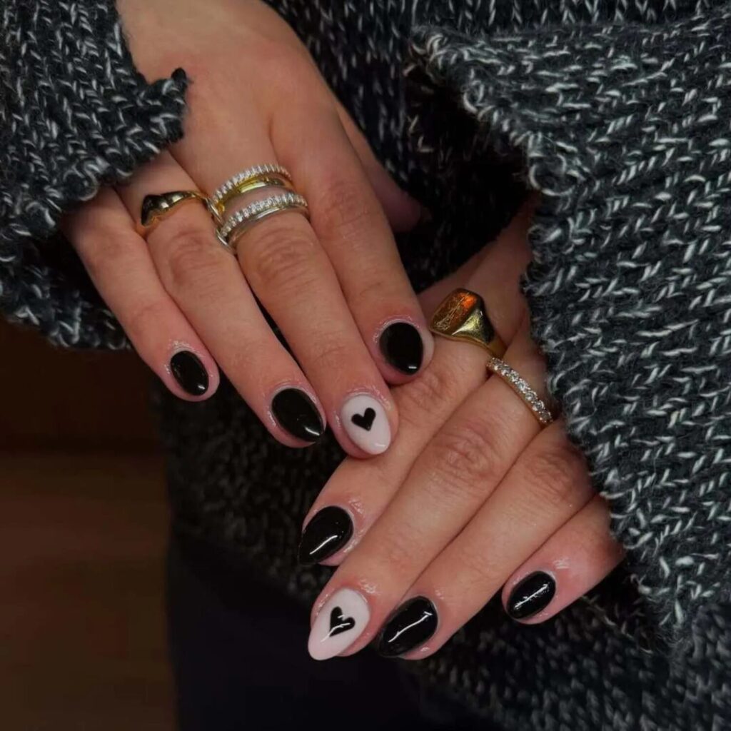 Closeup of short nails with black glossy polish and whimsical heart accented nail art adorned with rings