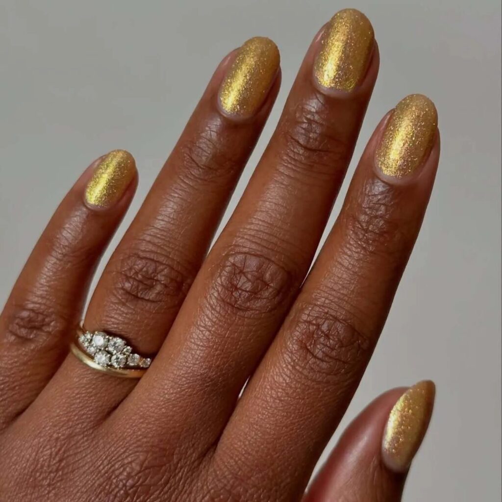 Short gold shimmer nails styled with gemstone rings simple reflective manicure with luxe vibes