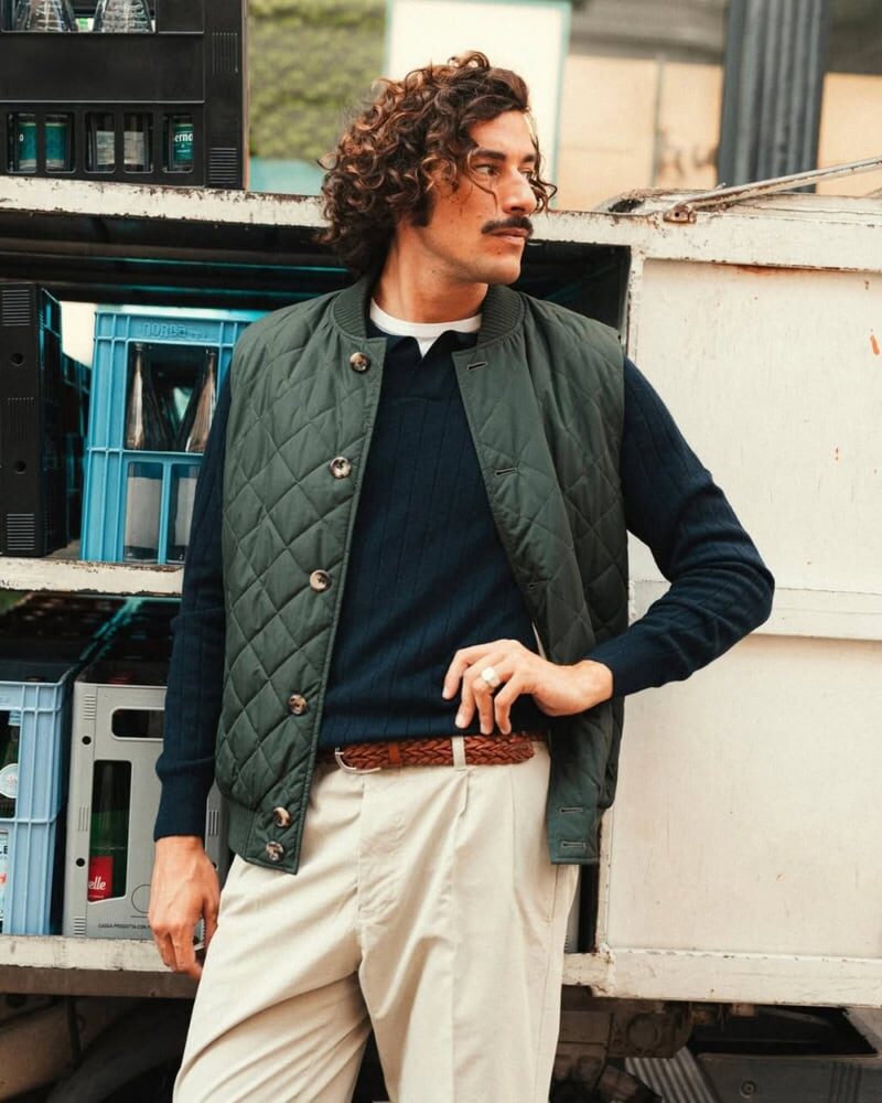 man wearing black padded vest over sweatshirt and jeans walking outdoors