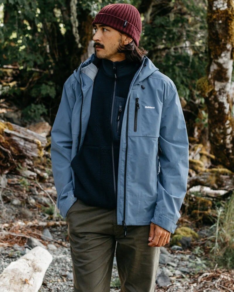 man wearing navy technical shell jacket layered over hoodie and jeans in rainy fall day