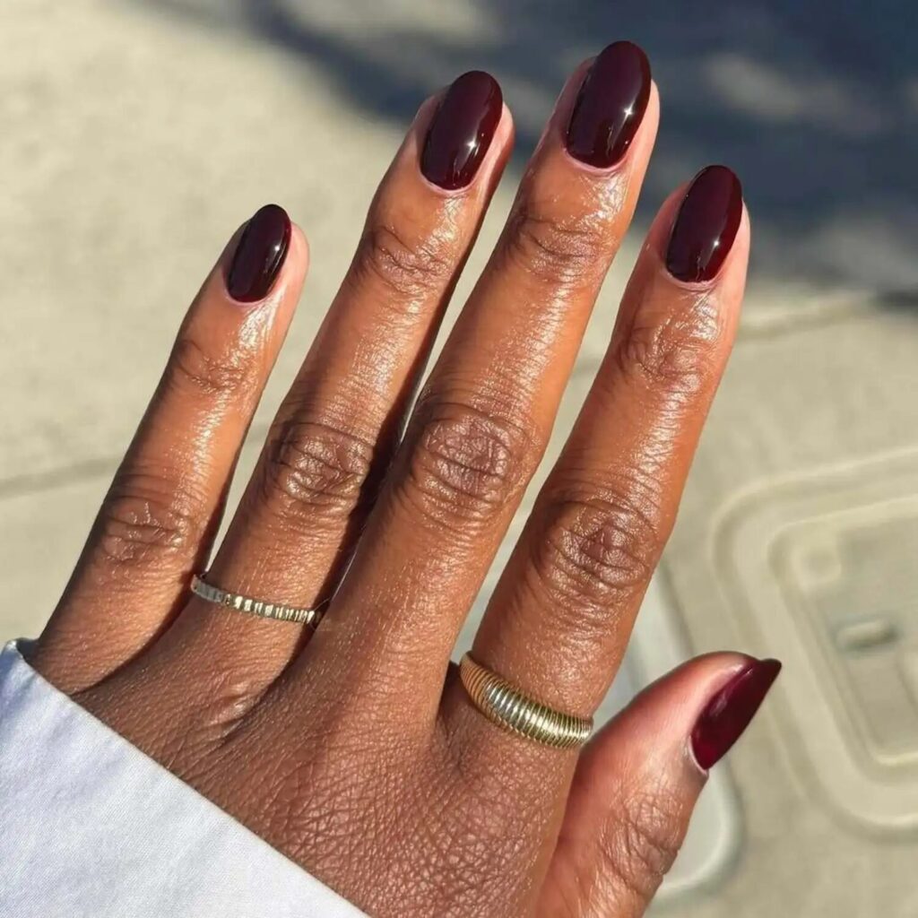 Short burgundy cherry cola nails styled outdoors with rings elegant fall manicure