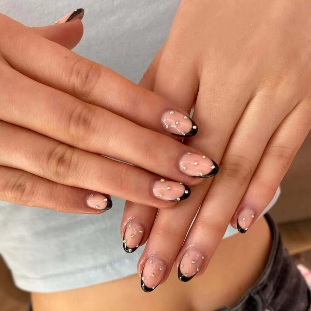 Short nails with black French tips and studded accents for a bold edgy manicure