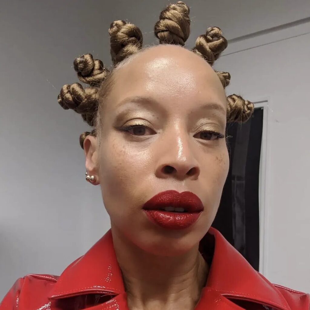 Woman with sleek classic Bantu knots wearing a neutral fall outfit and glowing natural skin