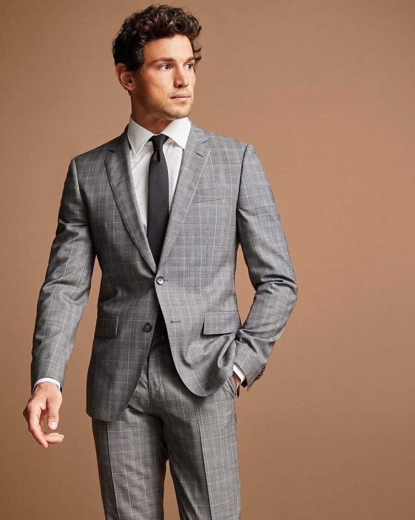 Man dressed in Hugo Boss slim fit checked virgin wool suit, standing confidently in urban office background.