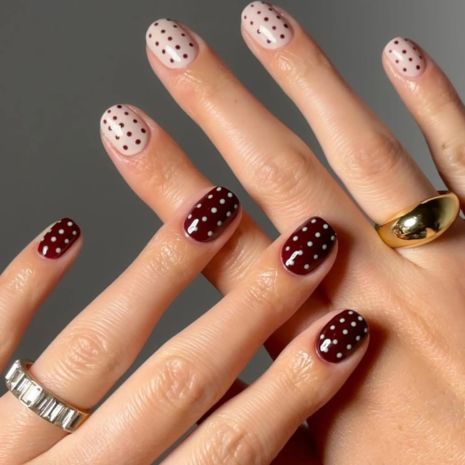 Short nails with cream and burgundy polka dots for a retro yet modern minimalist manicure.