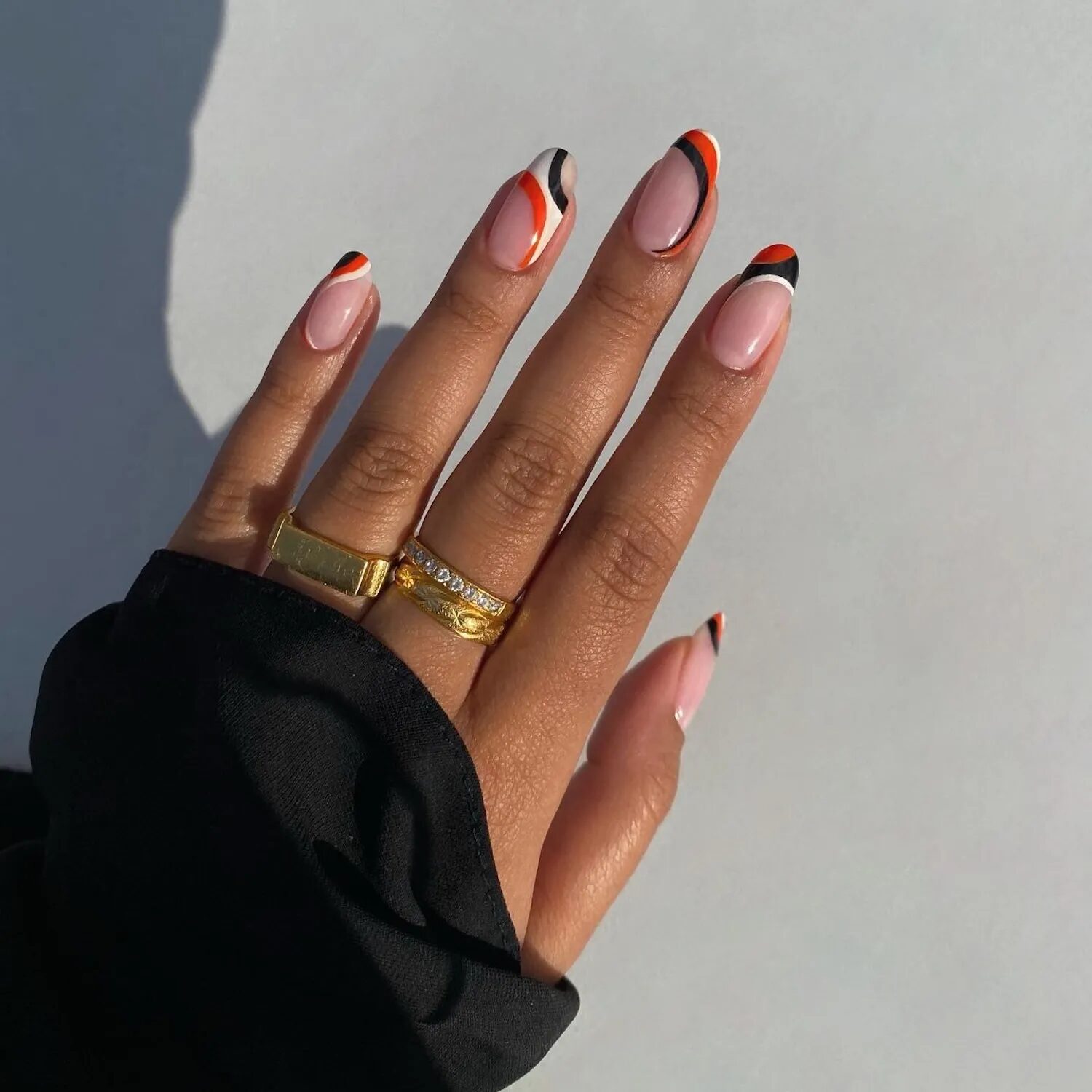 Close-up of orange, black, and white swirl French manicure with modern Halloween design.