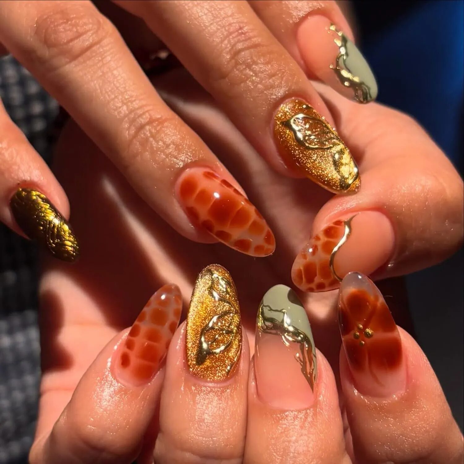 Amber and terracotta velvet glass manicure with gold chrome accents and mismatched nail art.