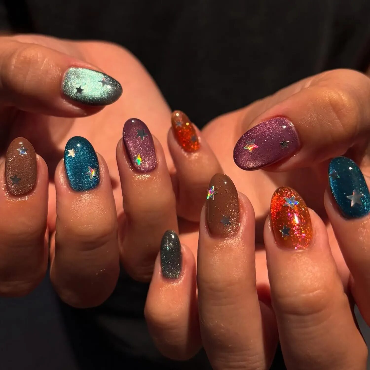Velvet glass nails in multiple colors with orange and star accents, cosmic nail design.
