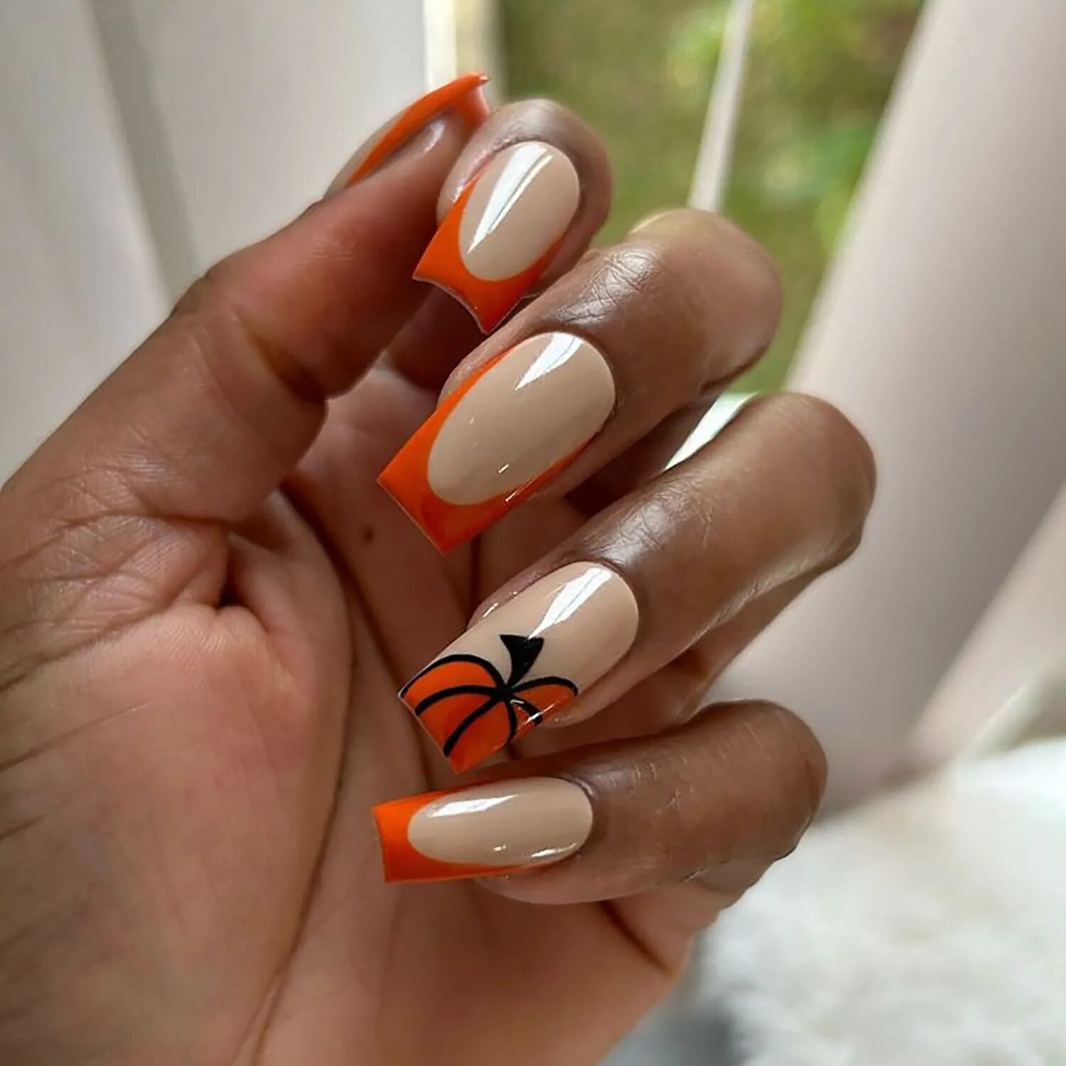 Nude nails with orange French tips and pumpkin accent for cozy Halloween-inspired manicure.