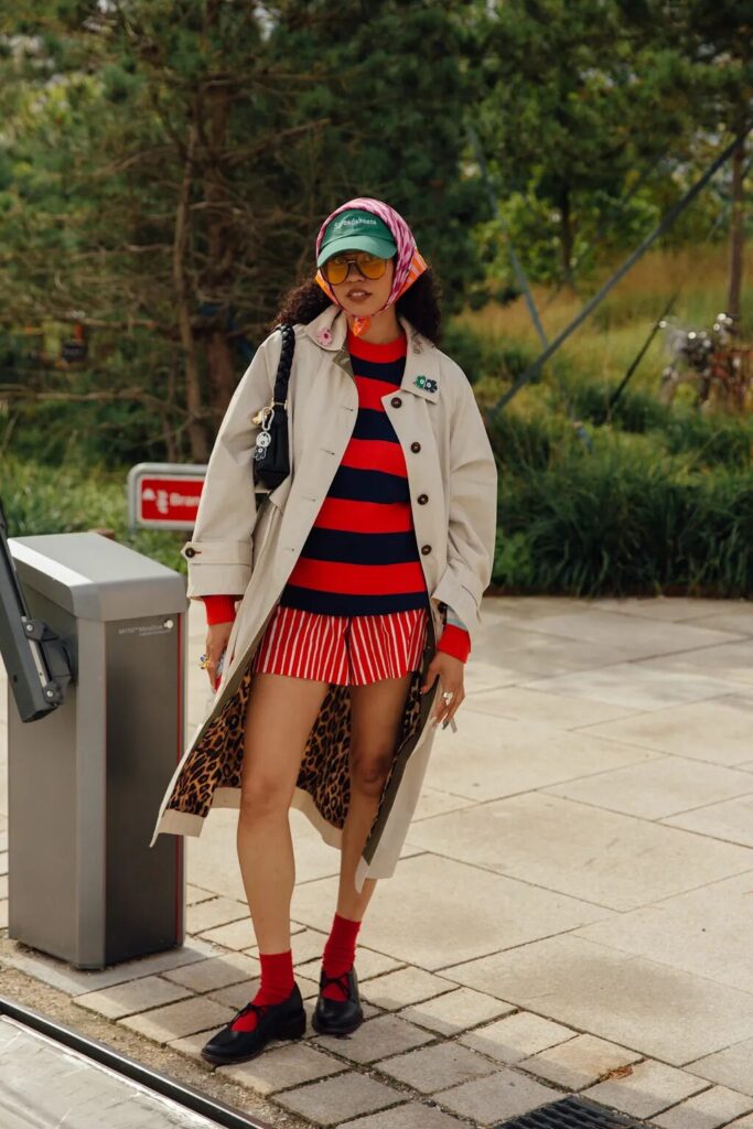 Street-style look with tailored shorts, striped sweater, and trench coat for transitional weather.