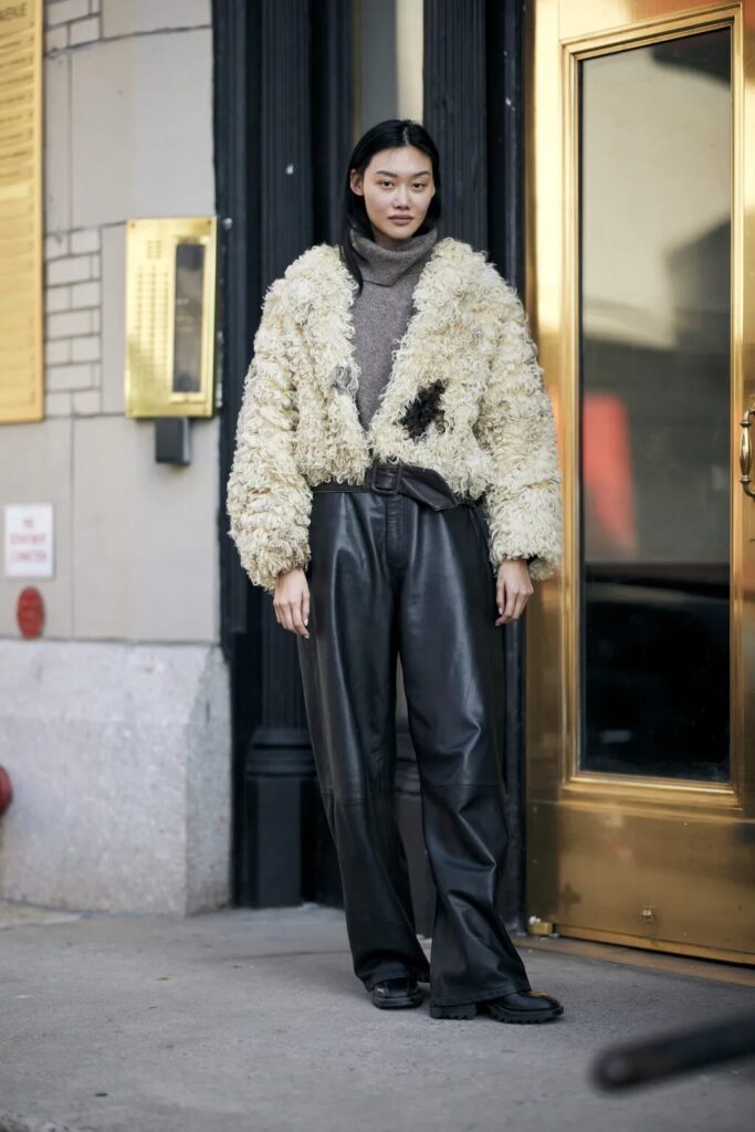 Fashion model in leather pants, cashmere sweater, and faux-fur coat showcasing luxe layering.