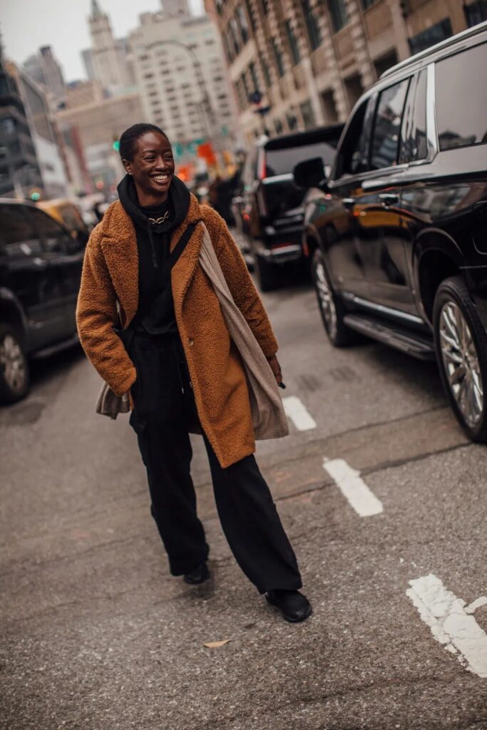 Hoodie layered under a teddy coat with sweatpants and sneakers for a relaxed fall look.