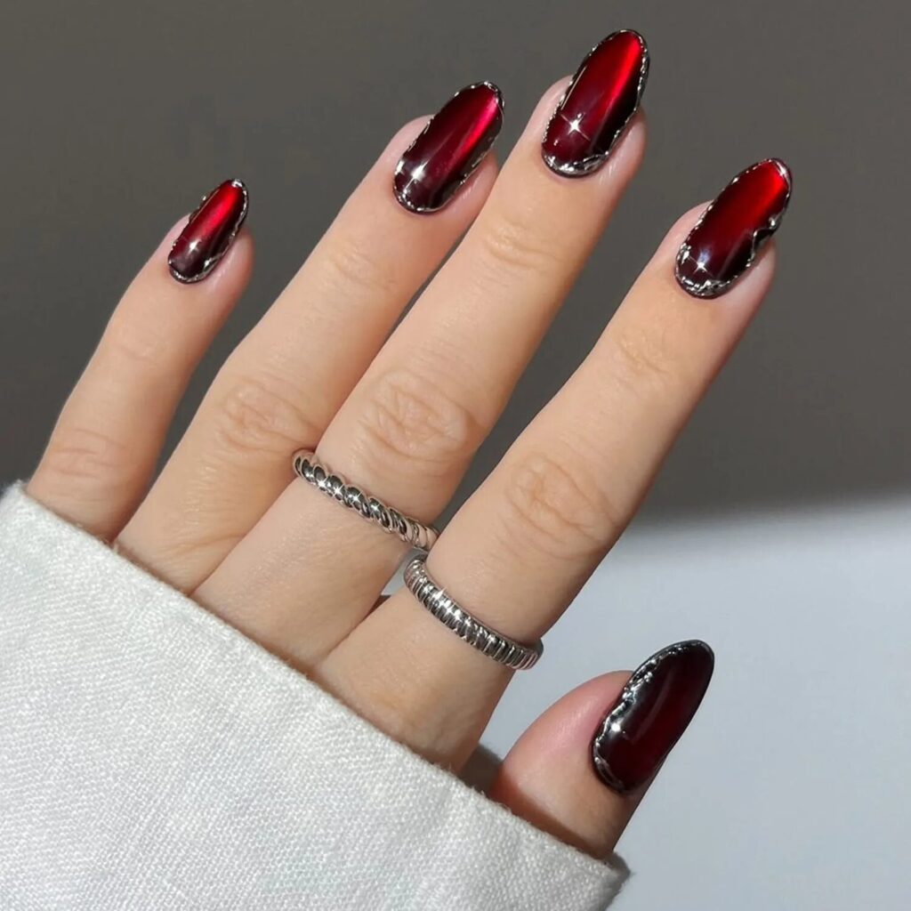 Close-up of deep red velvet nails glowing under warm light, exuding dark romantic energy