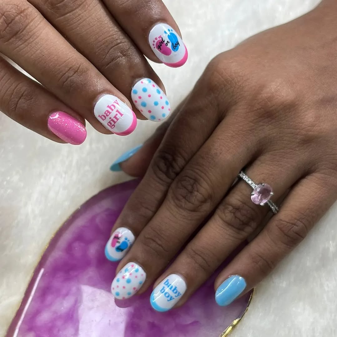 White nails with pink and blue polka dots and 'baby girl'/'baby boy' text