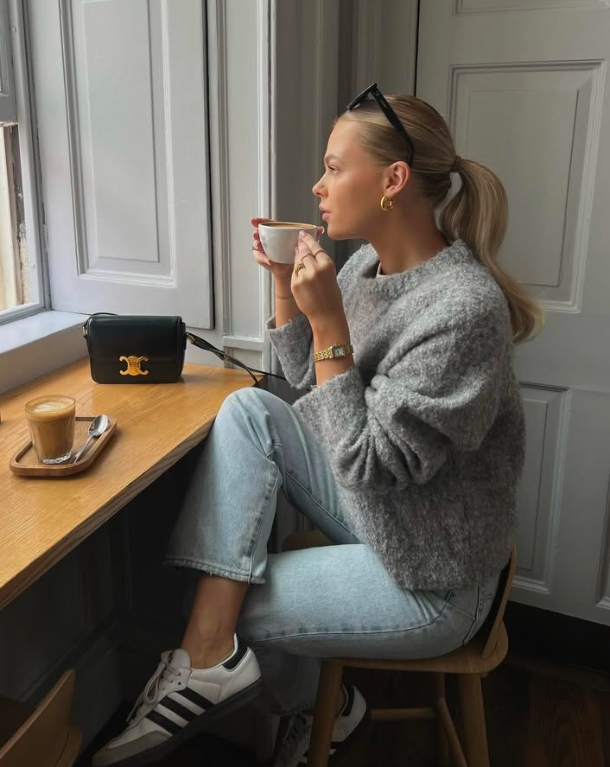 A soft knit and classic jeans against a backdrop of blooming trees.