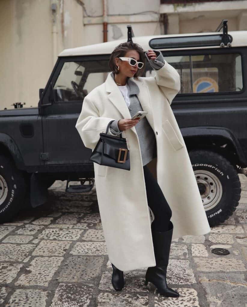 Woman wearing an ivory coat over grey layers with sleek boots, exuding city chic.