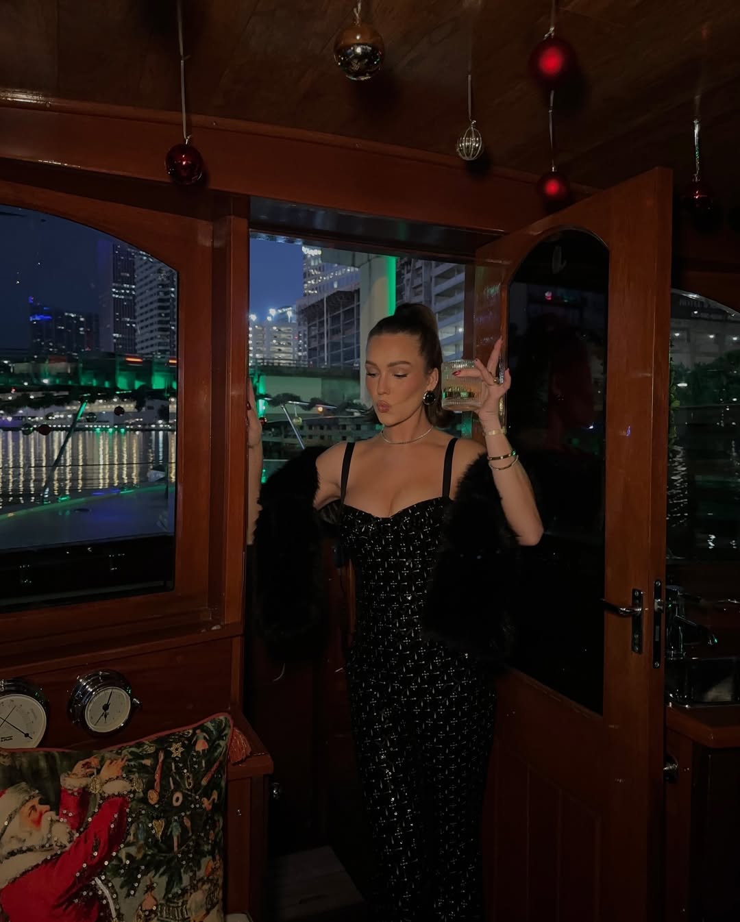 A sleek black dress paired with a fur stole, set against a city lights backdrop.