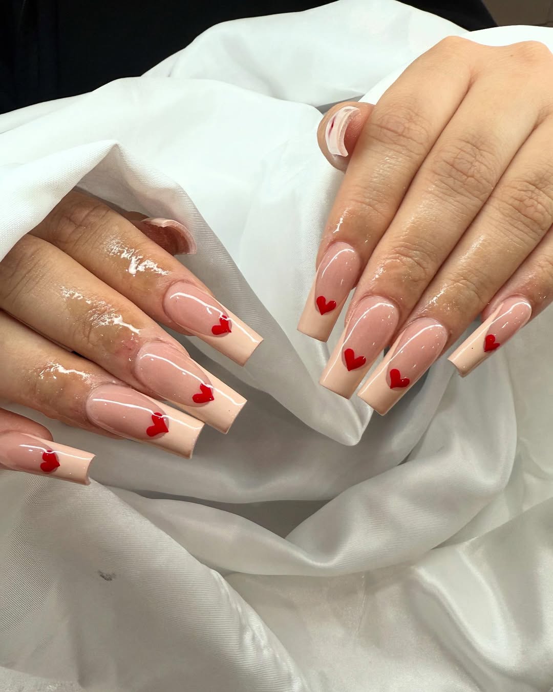 Clean nude nails with scattered tiny red hearts