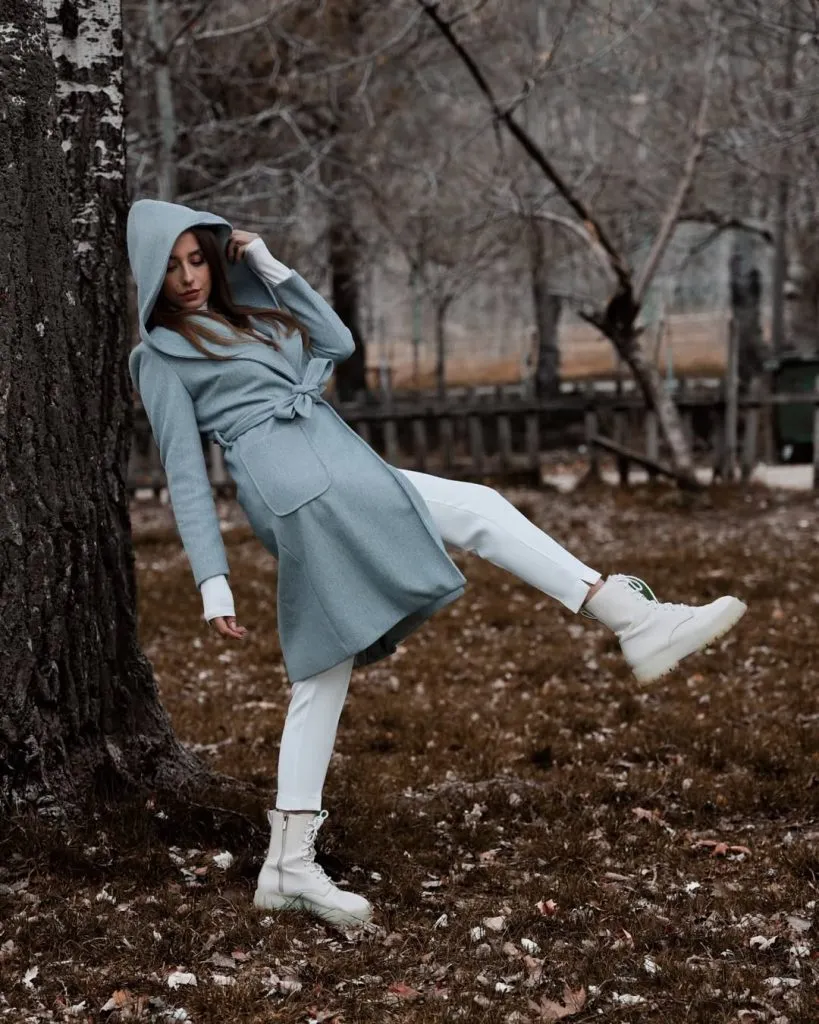 A woman wearing a soft pastel hooded coat with light-colored boots.