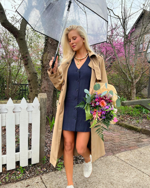 A trench coat, soft dress, and flowers for a charming rainy day look.
