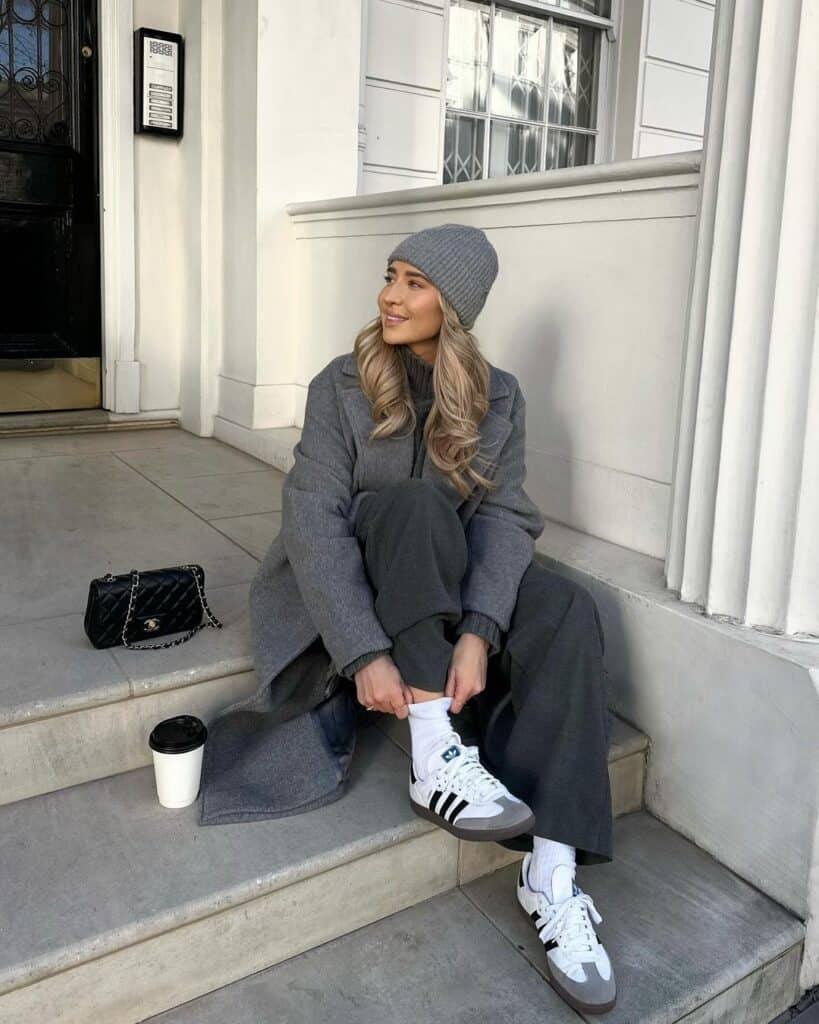 Woman in a grey-on-grey outfit with a long coat and sneakers, showcasing relaxed street chic.