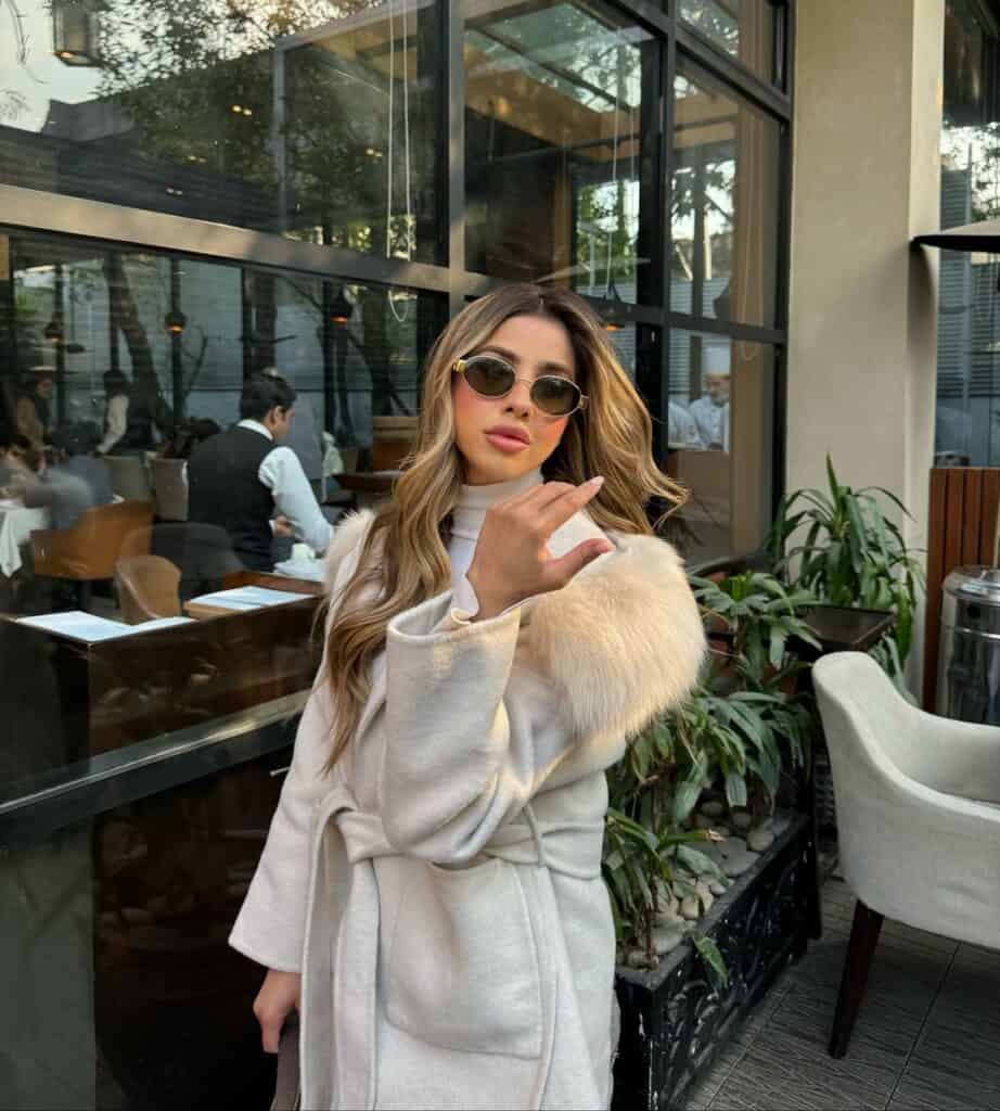 Woman in a neutral coat with subtle fur detail, exuding soft luxe style for a cafe outing.