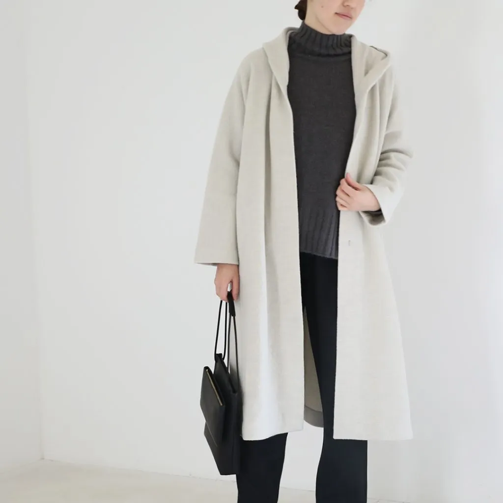 A woman wearing a light-toned hooded coat over darker layers, creating a minimalist aesthetic.