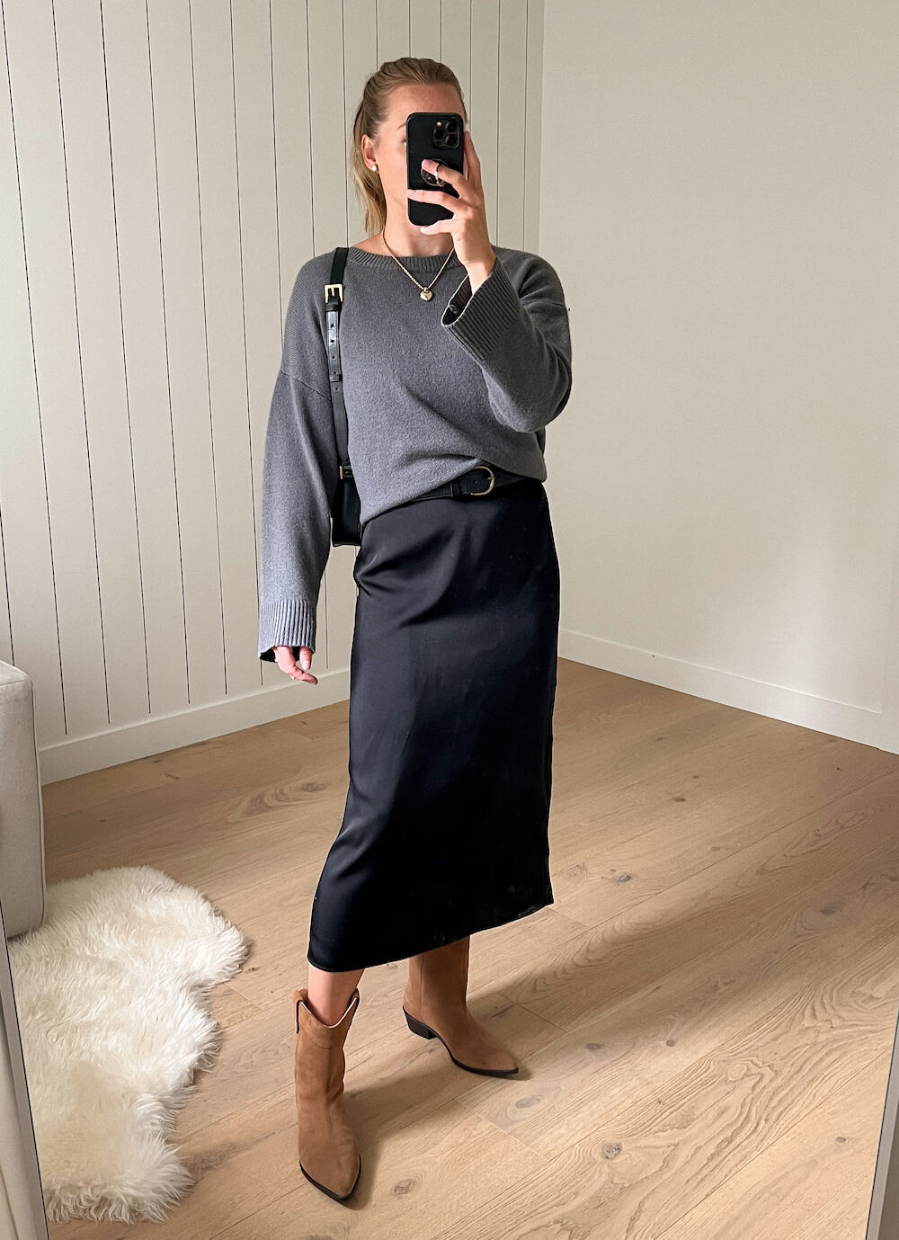 woman wearing a grey cashmere sweater over a long black slip dress with brown suede western style boots