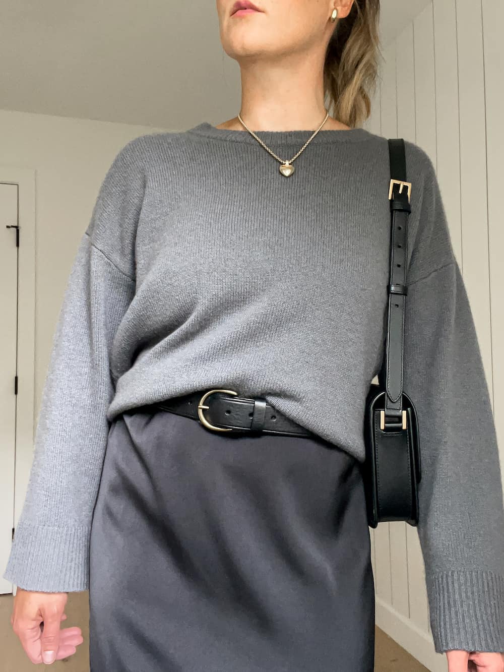 woman wearing a cashmere sweater over a black slip dress with a black leather belt