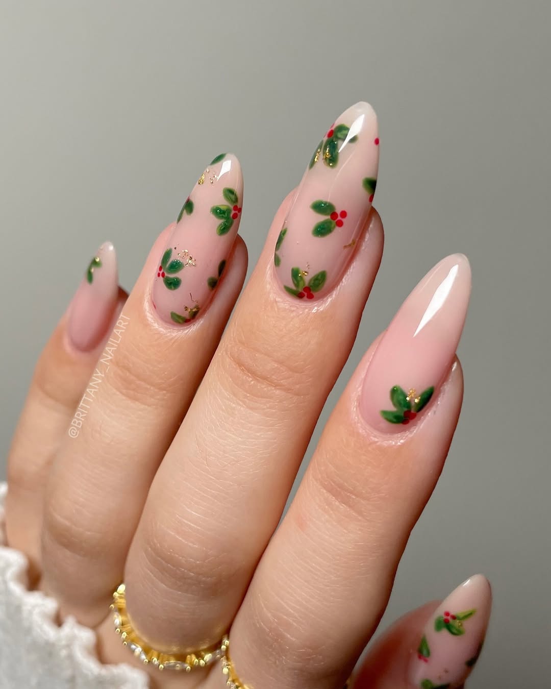 Translucent pink nails with scattered miniature holly sprigs and subtle gold flecks.