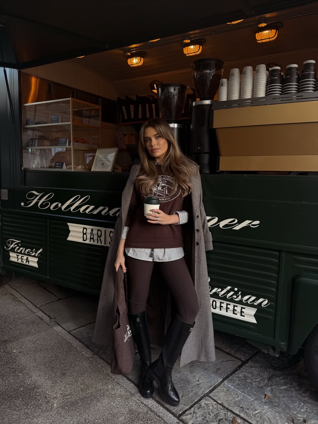 Woman in a houndstooth coat over layered brown pieces with riding boots.