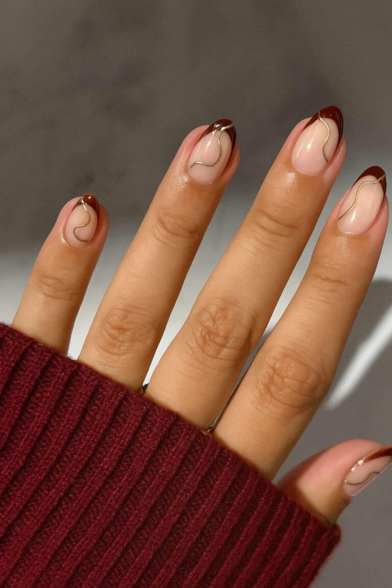 Burgundy nails with glossy nude base and gold squiggle detail