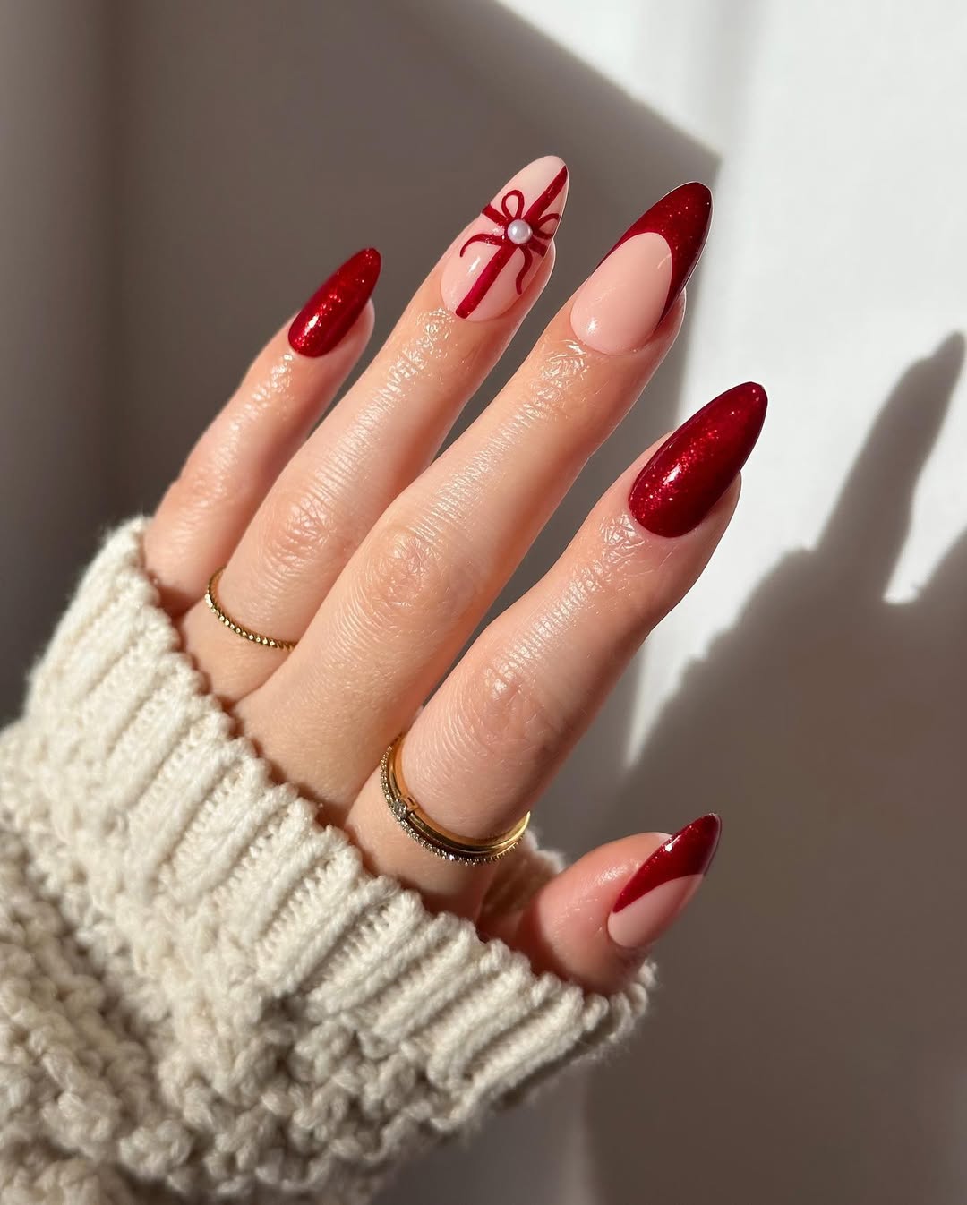 Almond-shaped nails with deep red glitter and a nude accent nail featuring a gift bow.