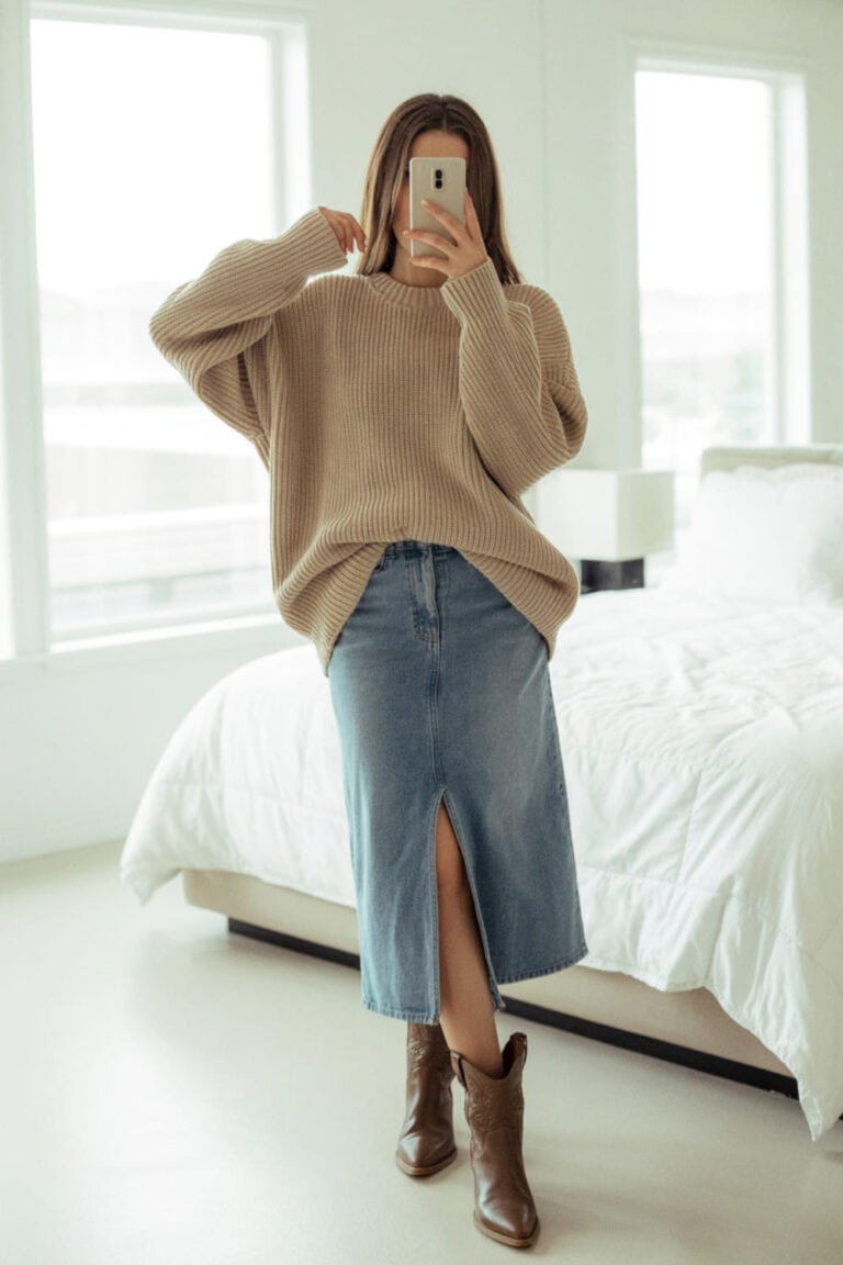 A person wearing a denim midi skirt with a slit and cowboy boots, paired with a chunky knit sweater.