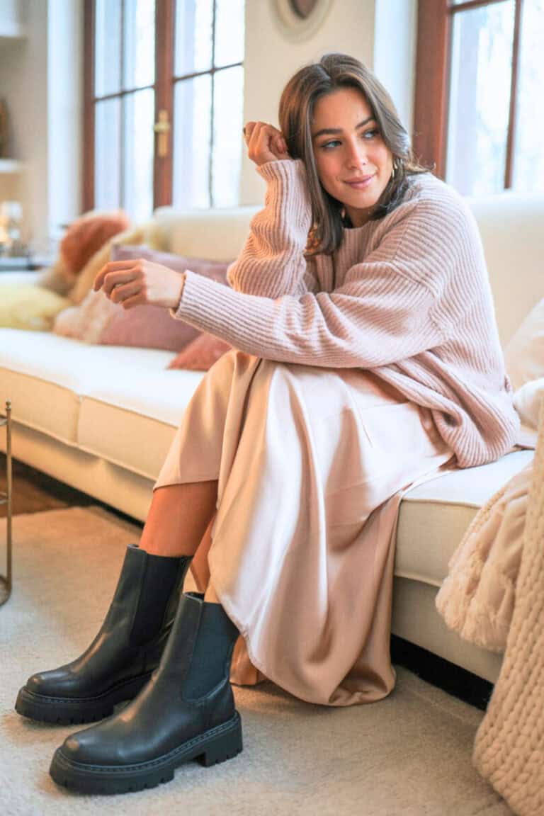 A person wearing a satin midi skirt with an oversized sweater and chunky ankle boots.