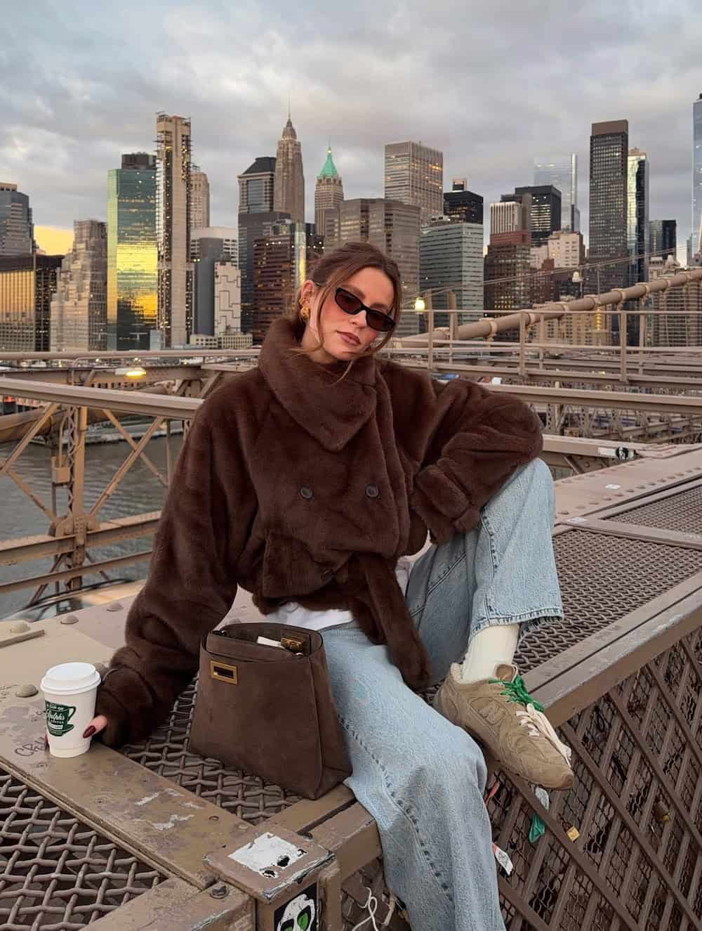 a woman wearing light blue jeans, a brown fur coat, and tan sneakers