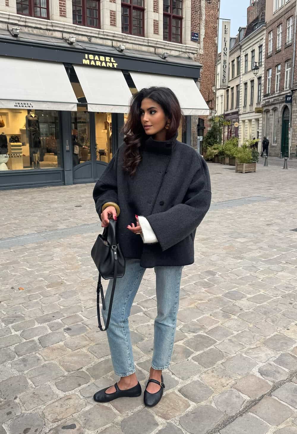 a woman wearing blue jeans, a buttoned coat, and mary jane sandals