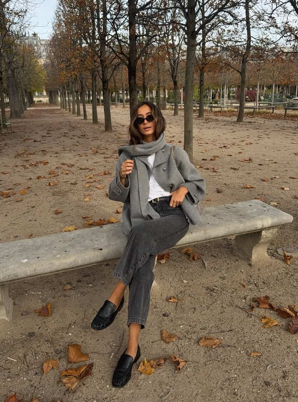 a woman wearing light black jeans, a white top, a grey scarf jacket, and black loafers